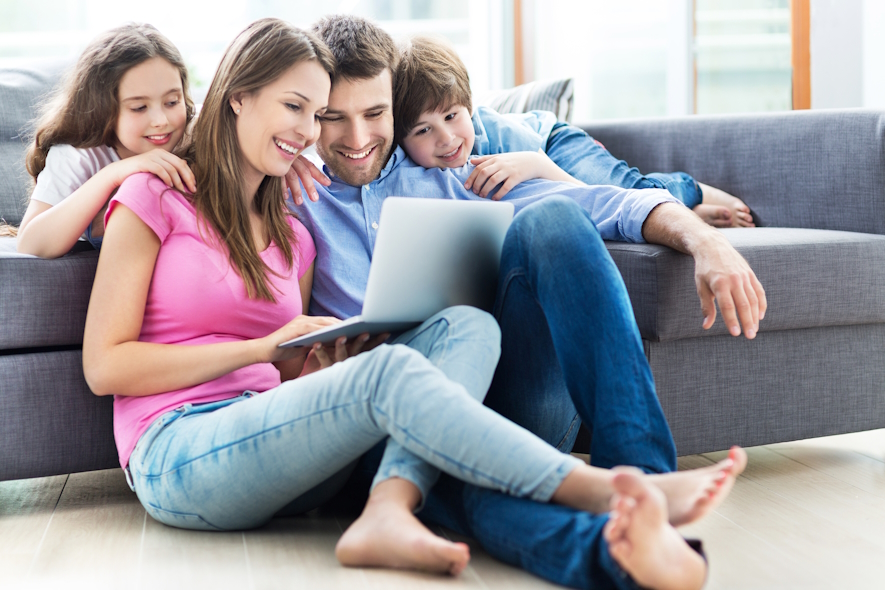 kids on a couch leaning on parents who are on the floor looking at a laptop.